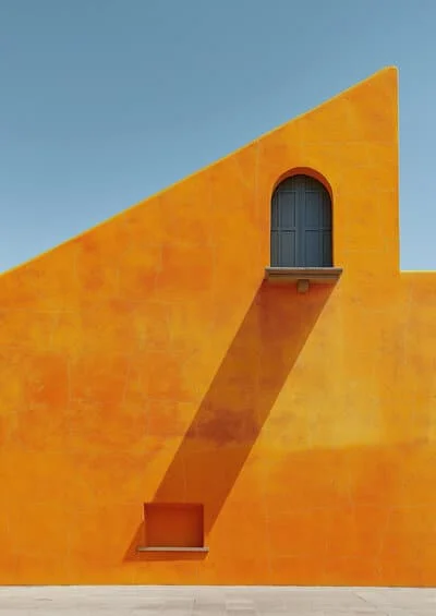 Façade architecturale orange vif avec une fenêtre arquée et un long jeu d’ombre projeté, sous un ciel bleu clair