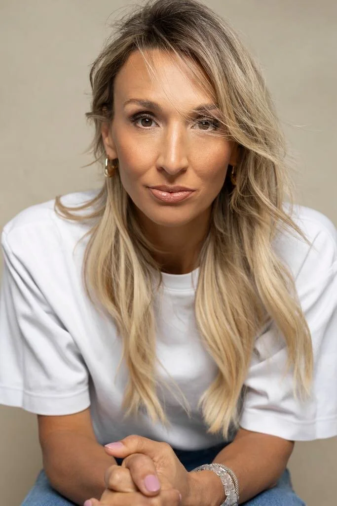 Portrait rapproché de Judith Fetzer en t-shirt blanc, les mains croisées, regardant l’objectif avec une expression confiante et posée