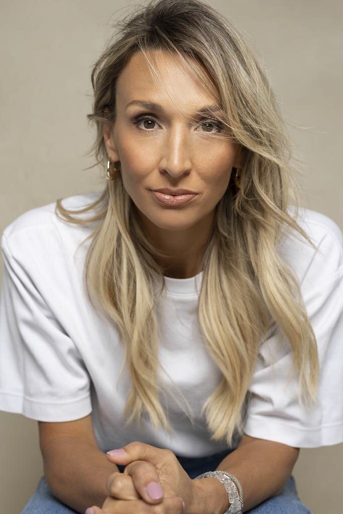 Portrait rapproché de Judith Fetzer en t-shirt blanc, les mains croisées, regardant l’objectif avec une expression confiante et posée
